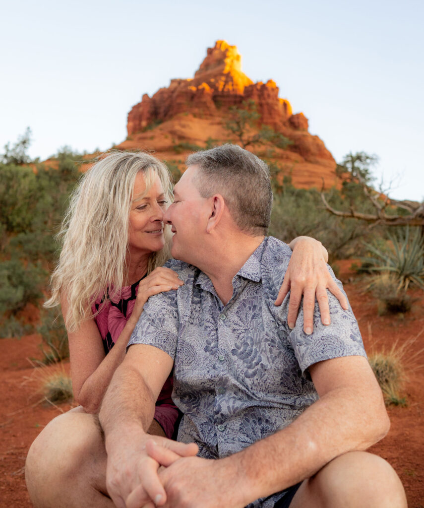 Male and female couple smiling and kissing with Sedona red rocks in the background