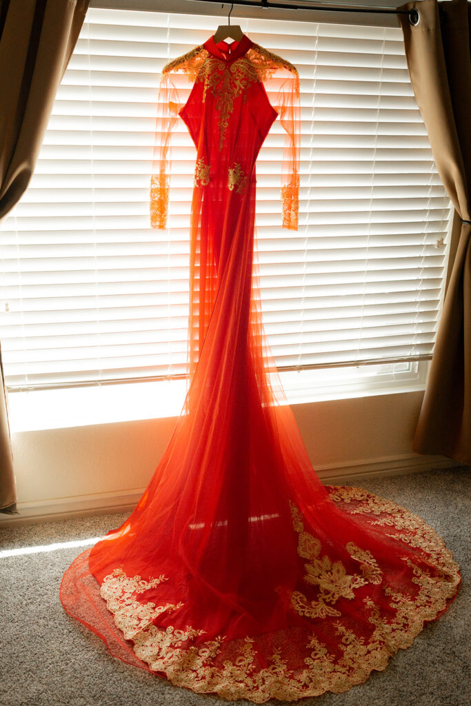 red wedding ao dai with gold lace and embellishments is hanging on a hanger in front of the mirror. The train is splayed out in front