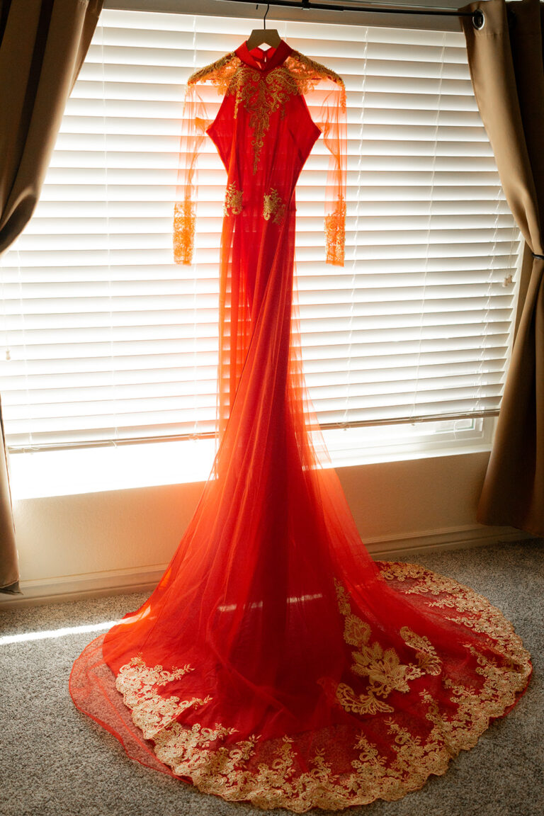 red ao dai with gold lace and embellishments is hanging on a hanger in front of the mirror. The train is splayed out in front