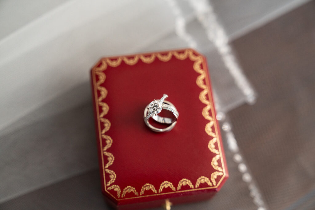 three rings on top of a red cartier ring box, on top of a veil