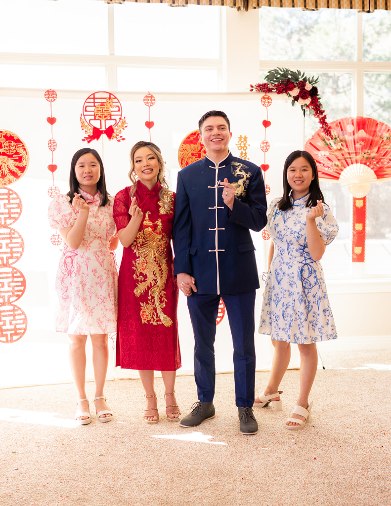 four people in chinese qipao and tang suit making heart fingers in front of a tea ceremony backdrop with heart fingers
