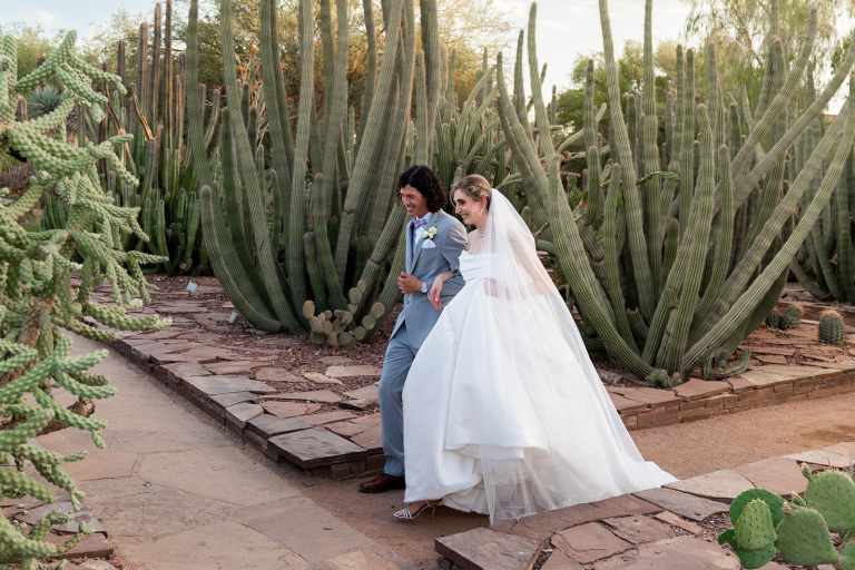 bride and groom arm in arm running through cacti in the desert