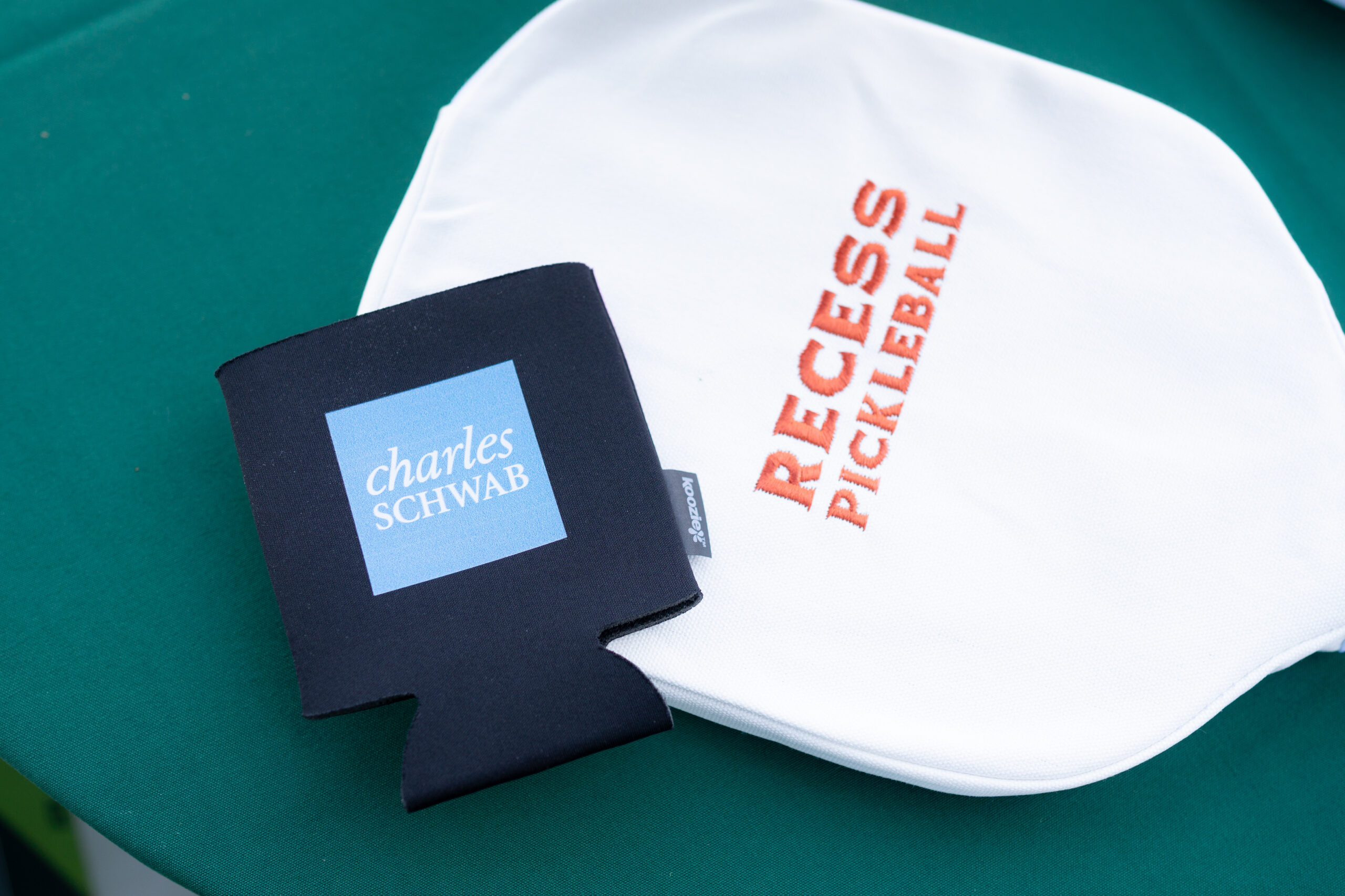 A black koozie with blue charles schwab logo and recess pickleball case