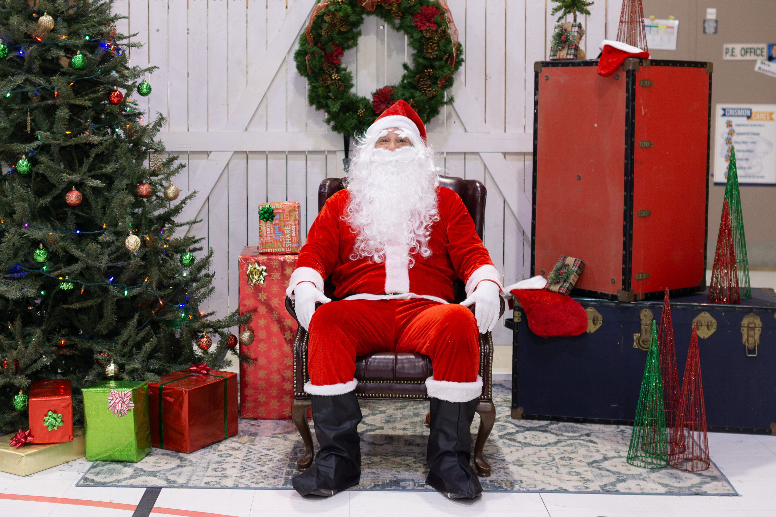 santa sitting on a chair smiling surround by presents and christmas tree
