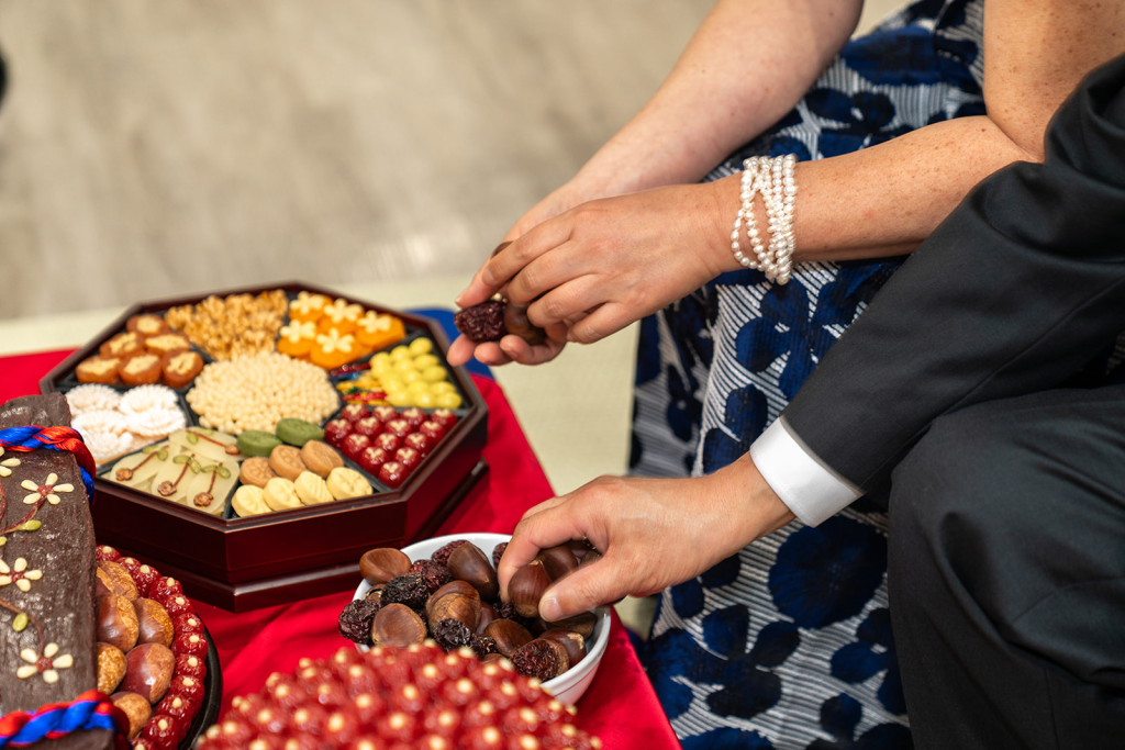 two sets of hands grabbing dates and chestnuts from traditional korean paebaek spread