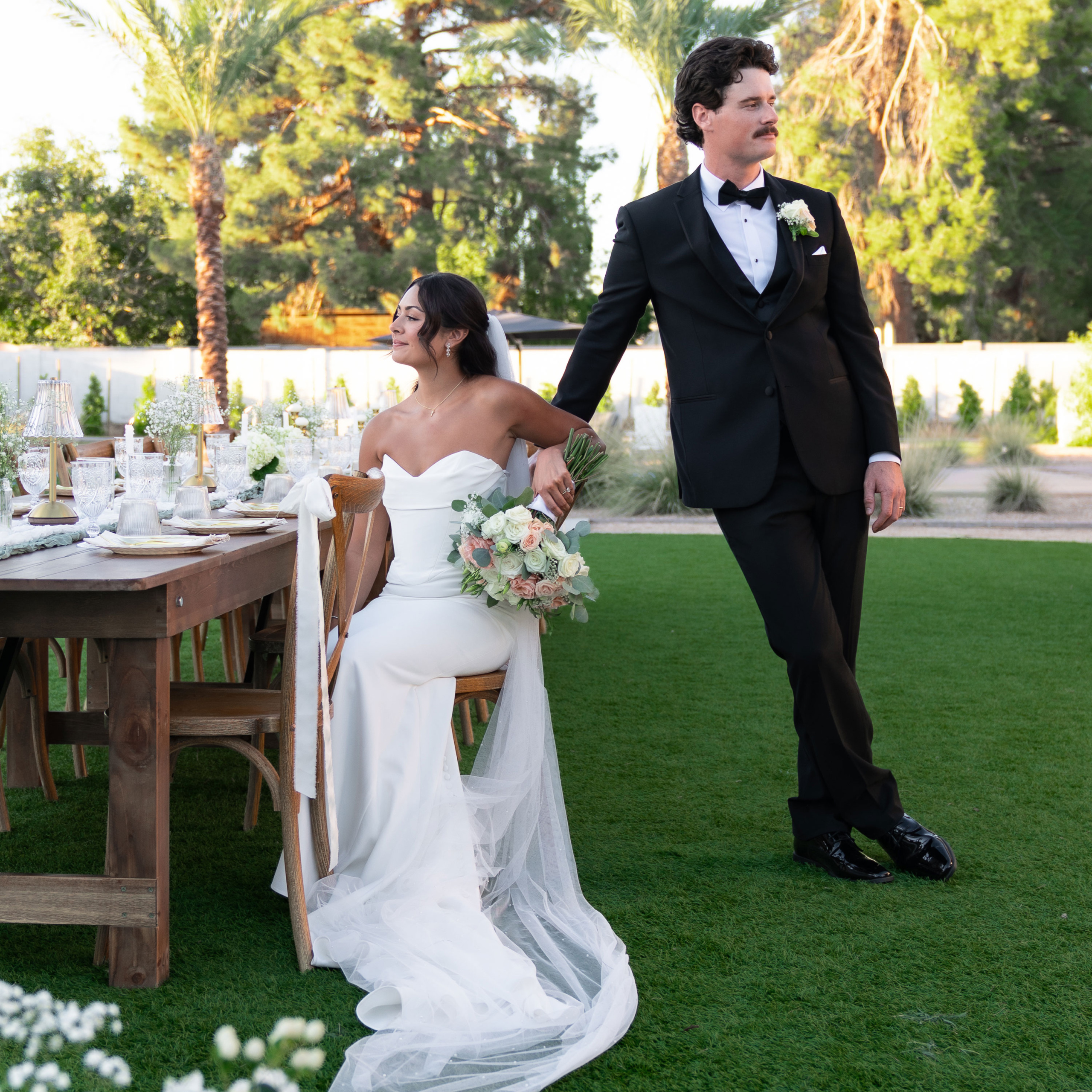 bride sitting at reception table and groom leaning up against chair scottsdale wedding
