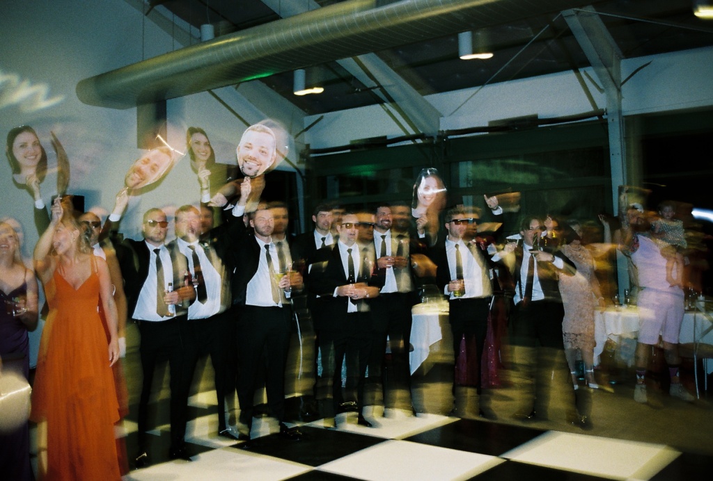 Wedding party dancing with cutout faces of groom during grand entrance checkered dance floor on film