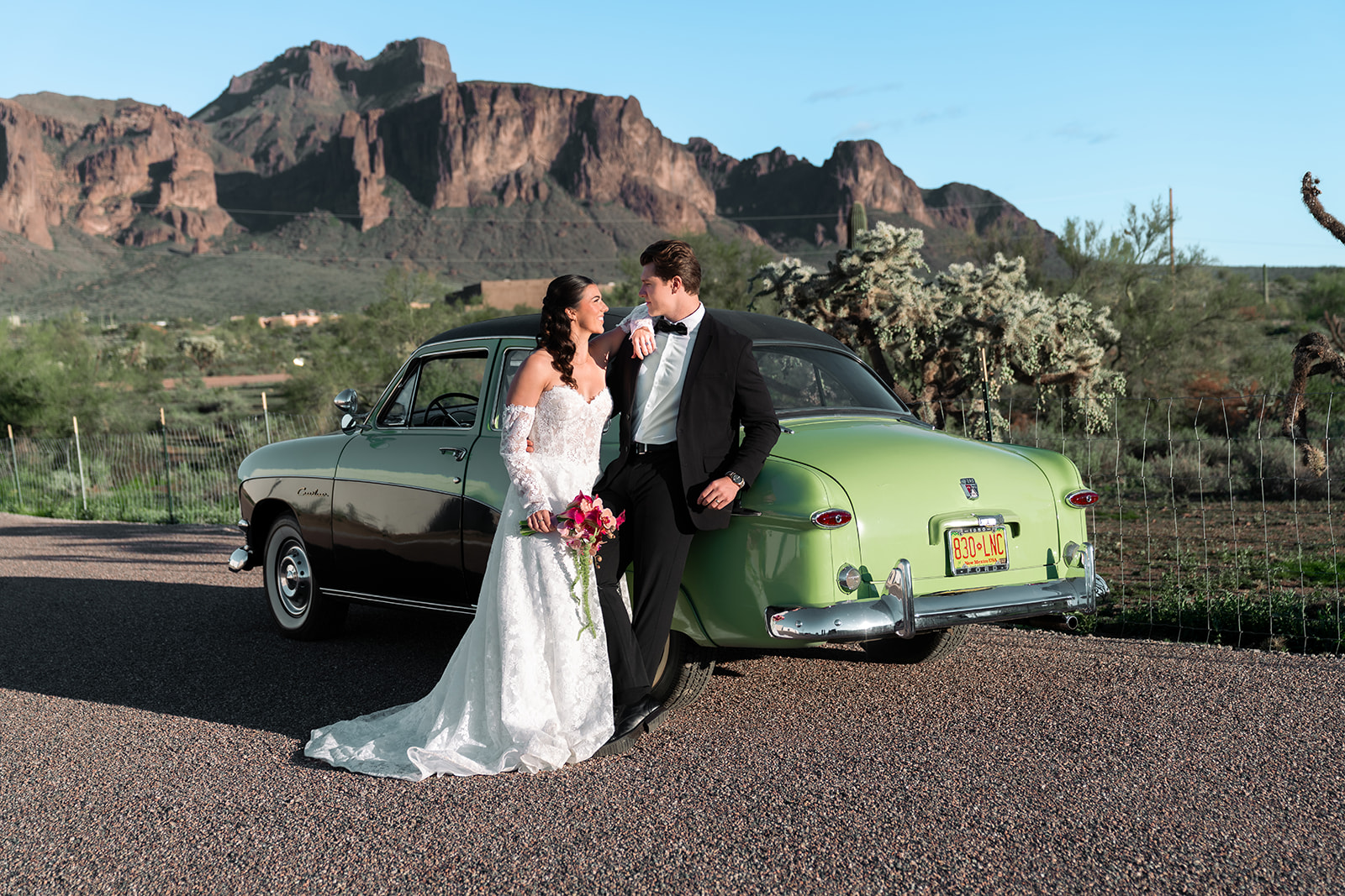 Bride and groom posing in front of a green Crestliner car in front of arizona superstition mountains