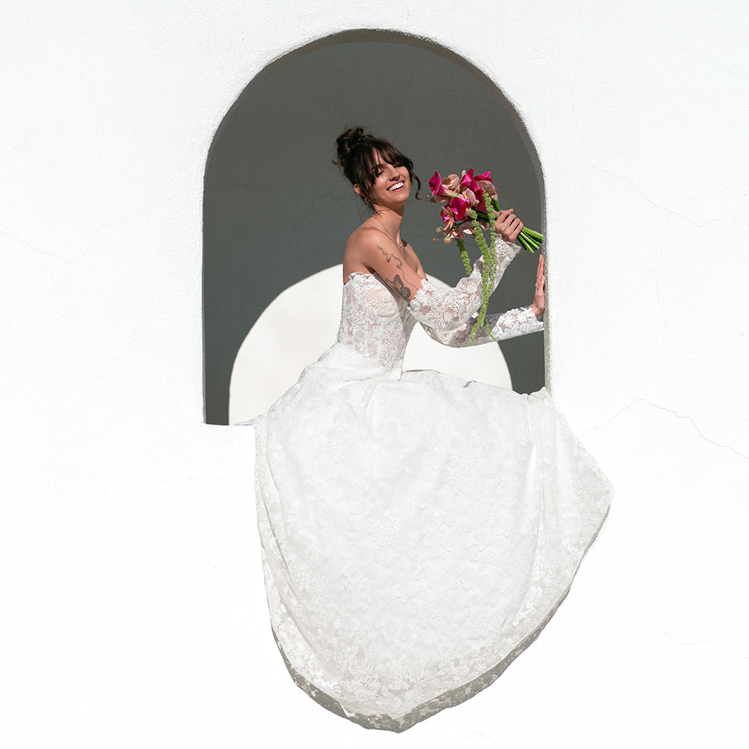 Bride sitting in an arched window holding a bouquet and smiling
