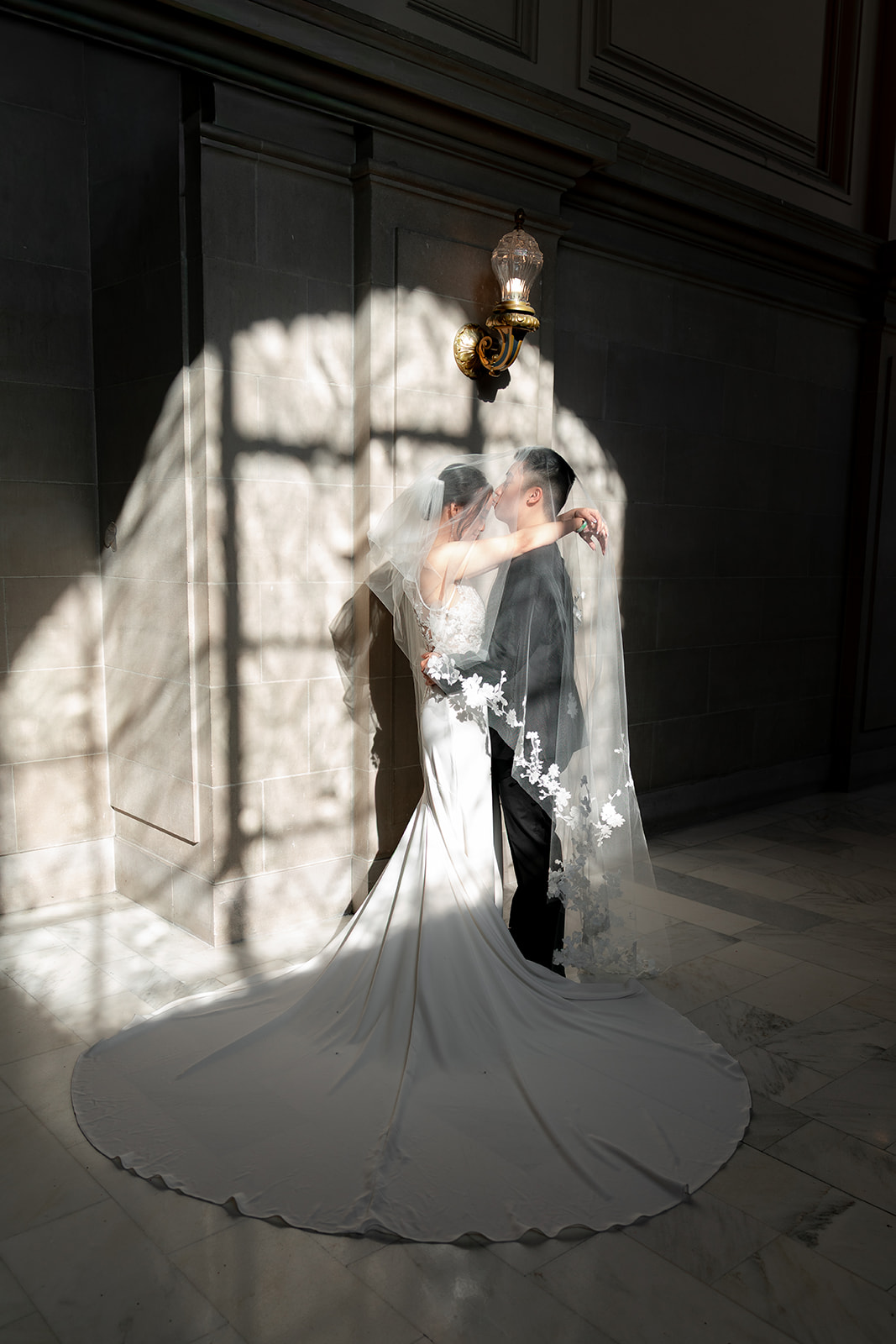 Bride and groom under veil at SF city hall with dramatic lighting