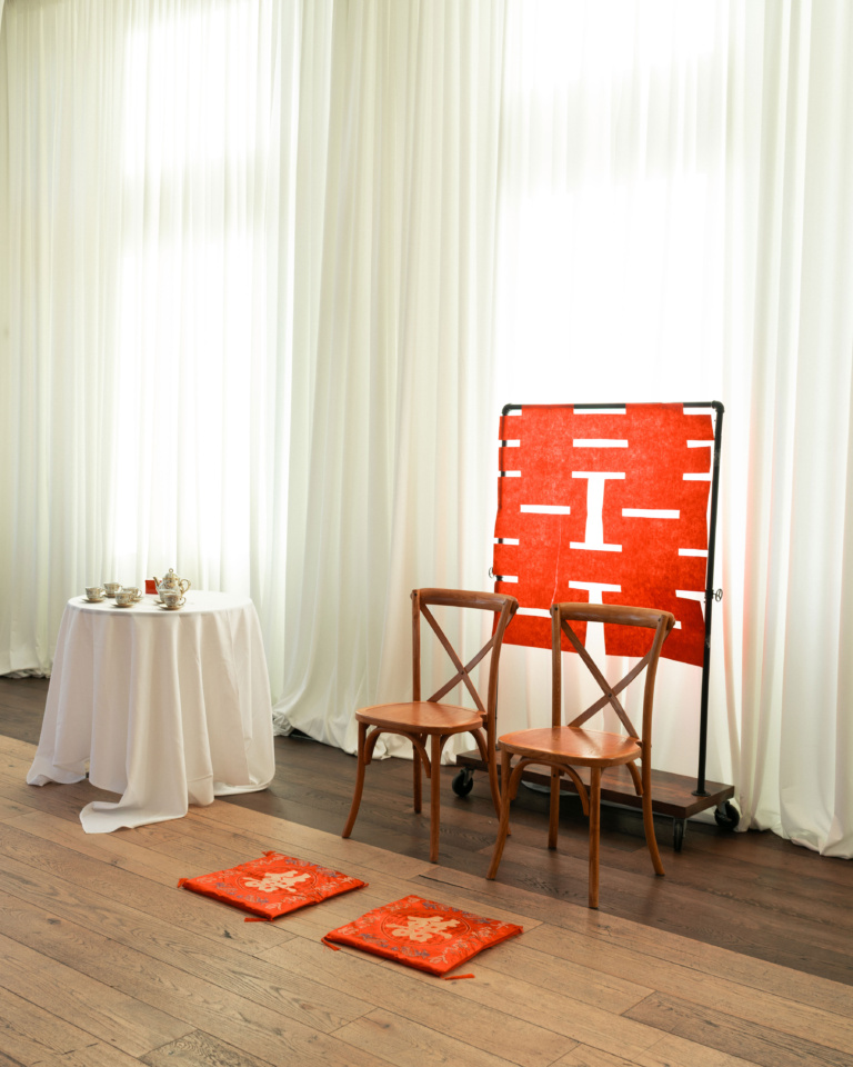 Tea ceremony setup with red double happiness symbol, two chairs, and two red kneeling cushions